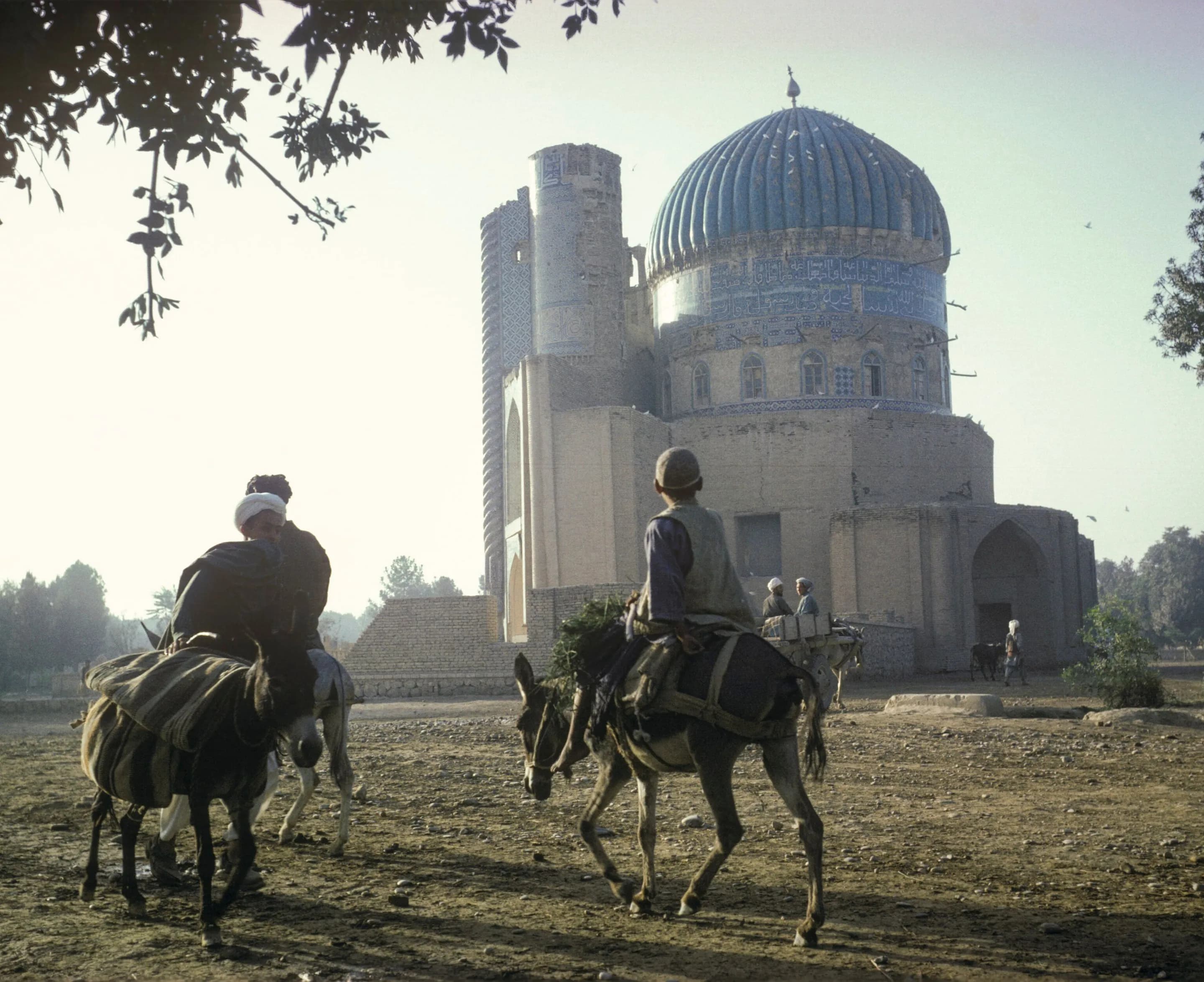 Riders on donkeys crossing the open ground in front of the blue-domed shrine of Khwaja Abu Nasr Parsa in Balkh, photographed by Herbert Maeder in 1969