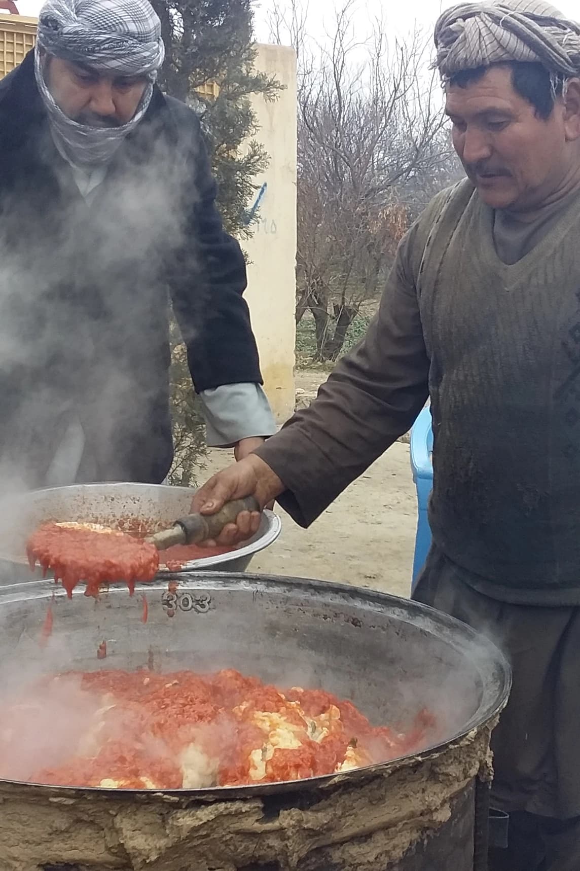 An Afghan cook preparing cauliflower in an outdoor pan