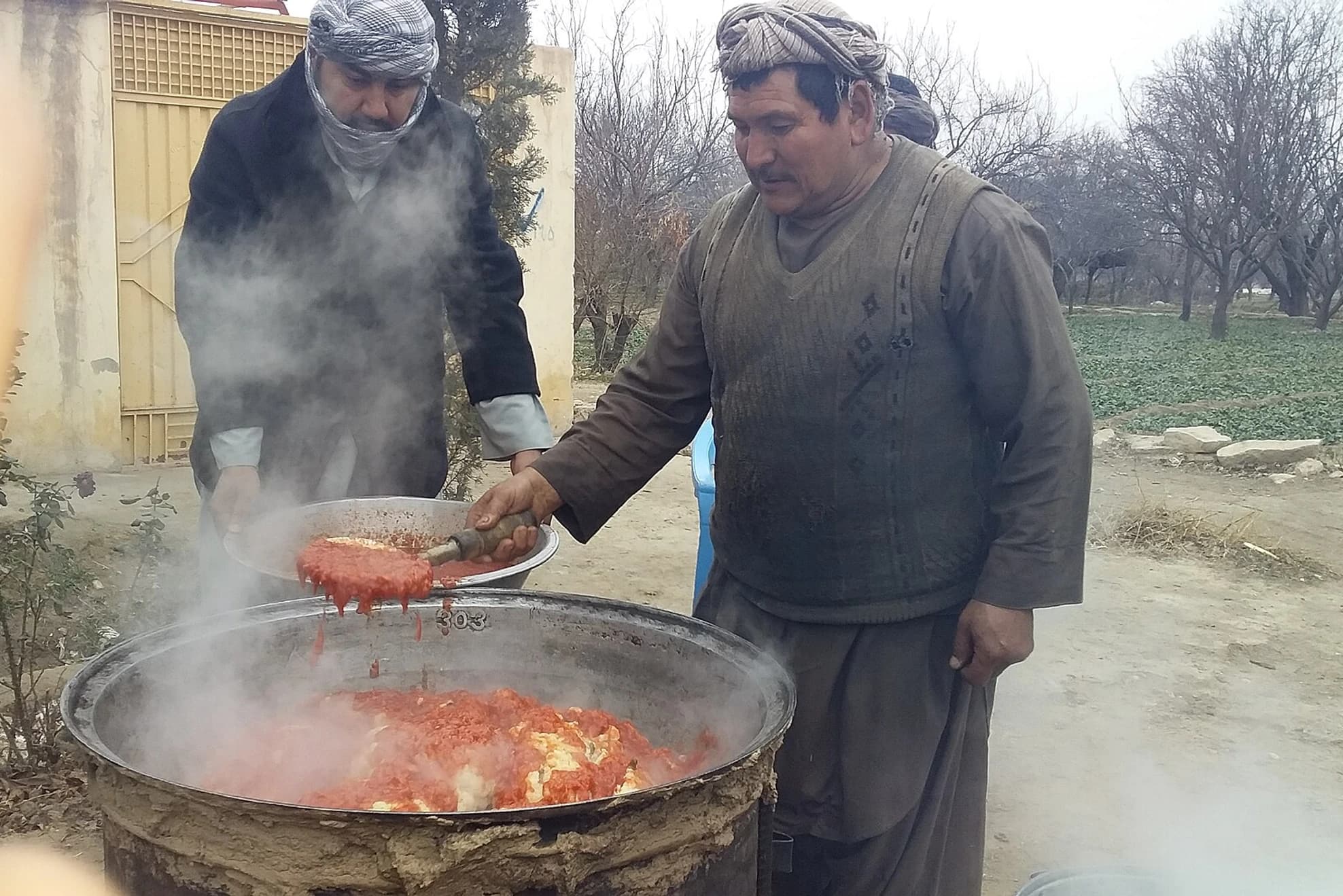 Afghan cooks preparing cauliflower in a large outdoor pan