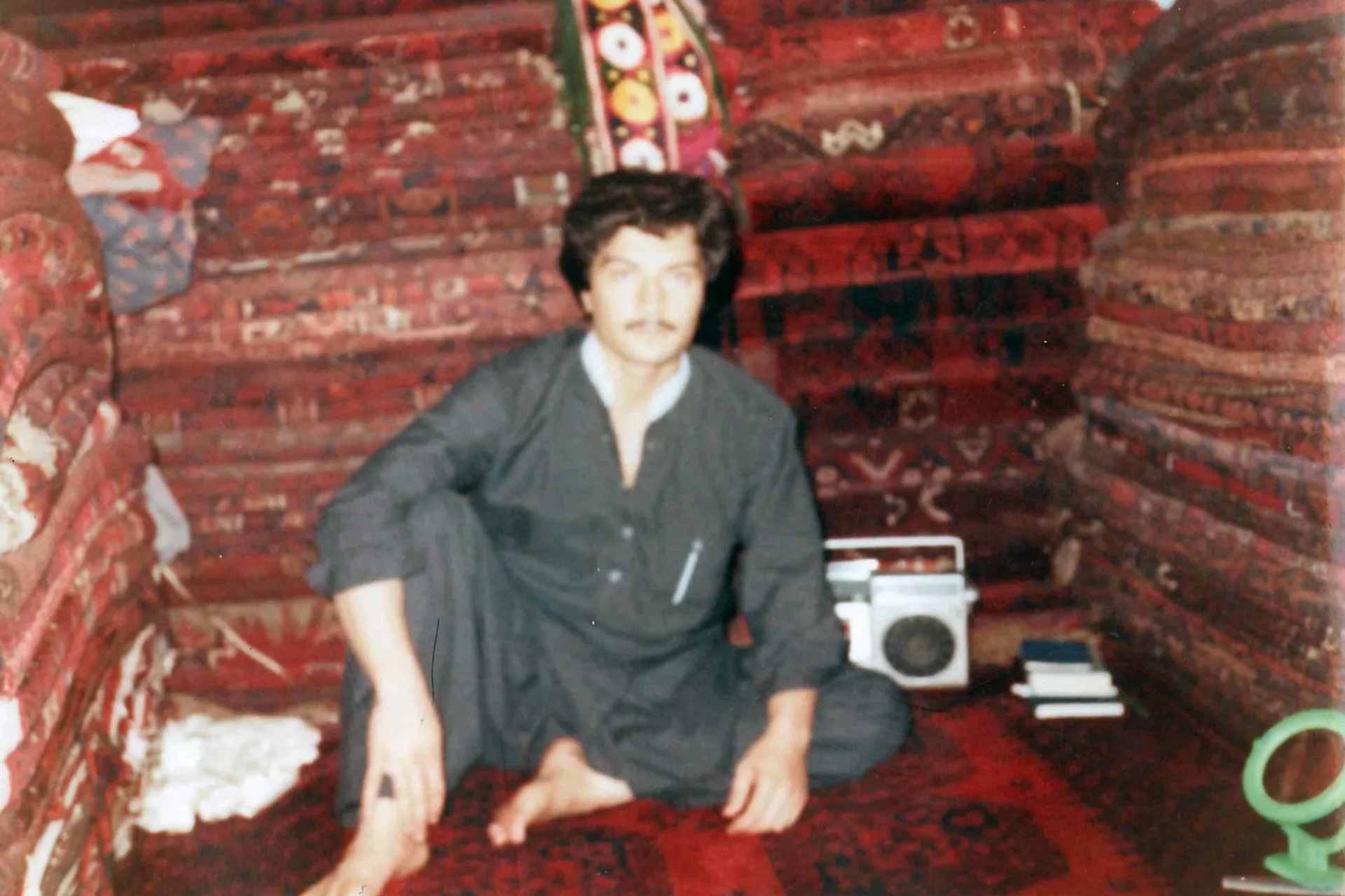 An Uzbek carpet seller sitting in his shop among stacked rugs
