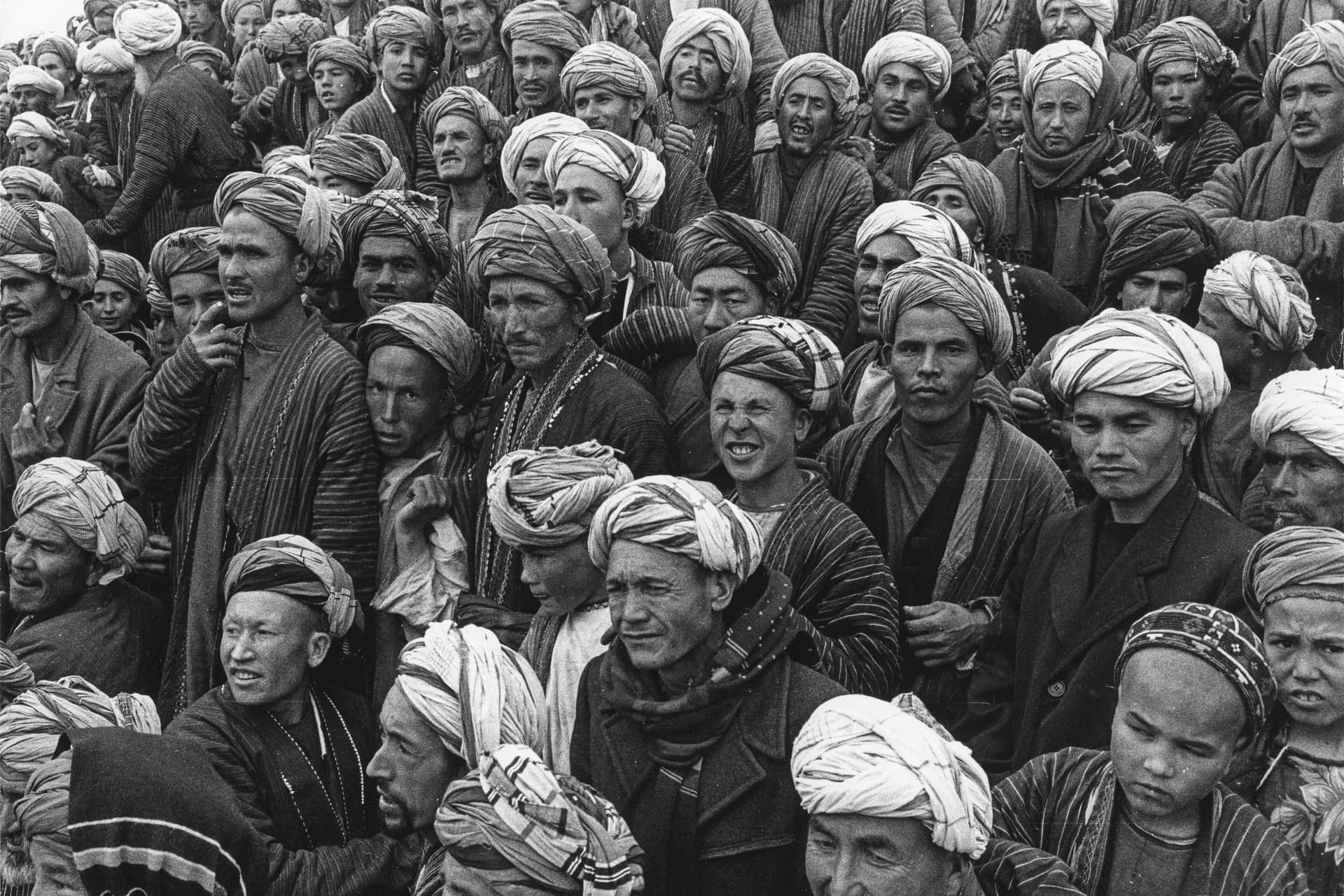 A crowd of men in white turbans and striped robes watching wrestling at the Eid al-Fitr festival in Aqcha, Jawzjan, photographed by Herbert Maeder in 1968