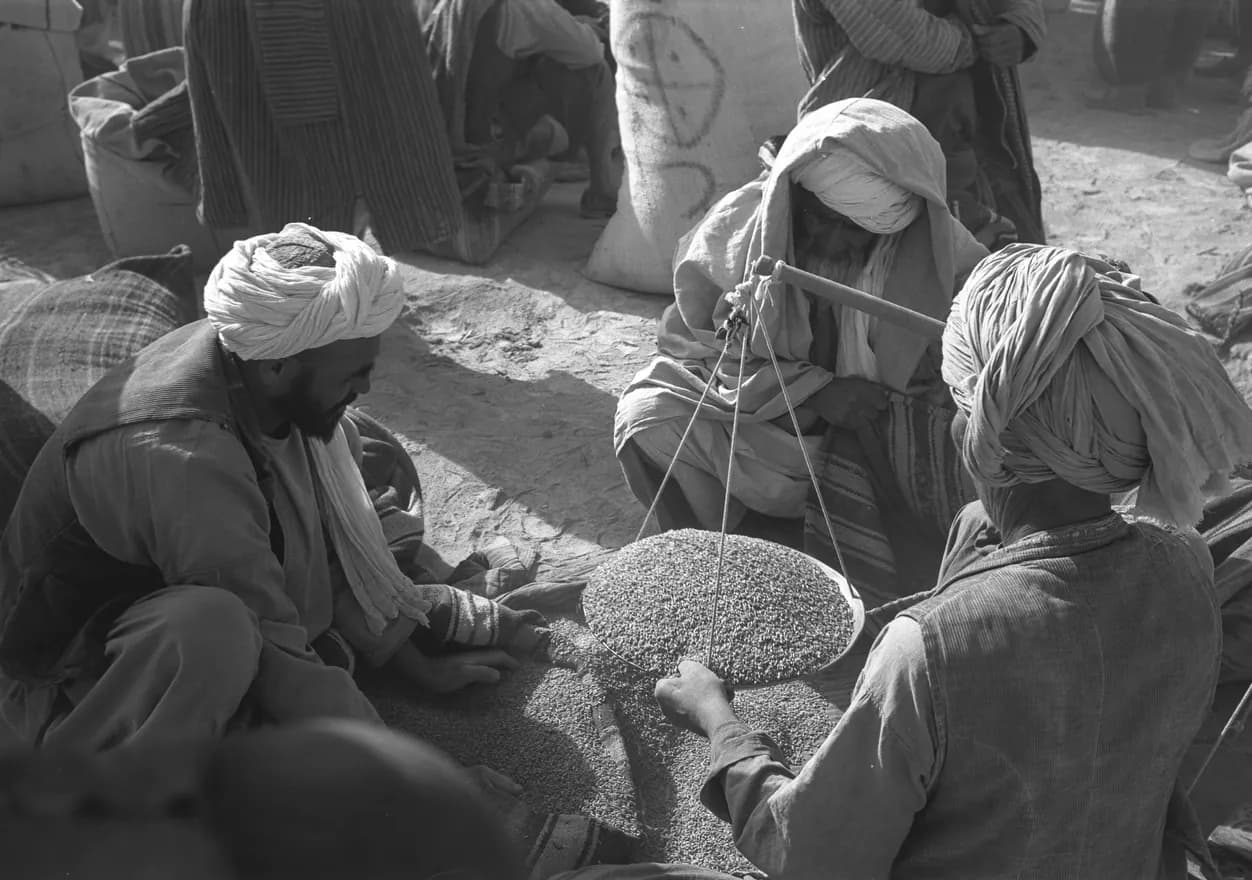 Traders seated around a scale at the grain market in Maimana, Faryab, 1969