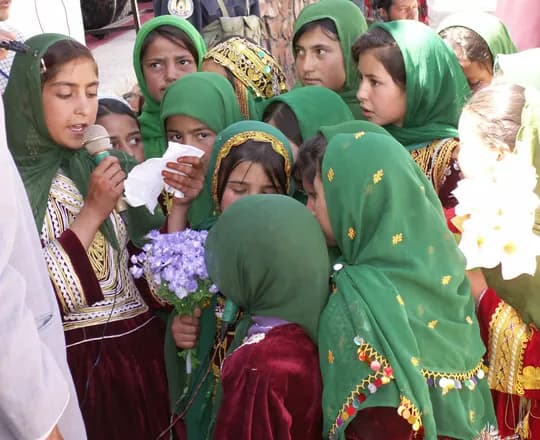 Girls in green scarves and embroidered red dresses singing at a gathering in Chaghcharan, Ghor Province, 2007