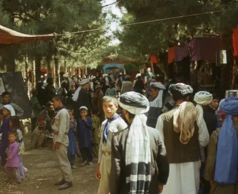 A festival crowd in turbans, scarves and holiday clothes beneath the trees in Khulm (Tashqurghan), Balkh, in 1976