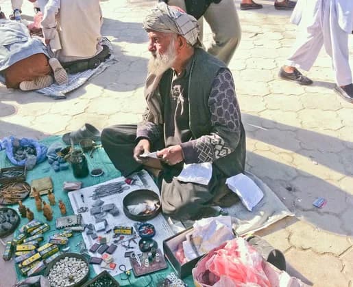 An elder in a turban and embroidered waistcoat selling goods on a cloth at the Nowruz gathering in Mazar-i-Sharif, Balkh, 2011