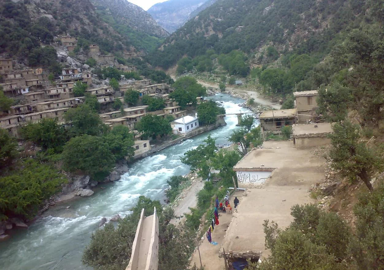 Stone houses stacked above a river and footbridge in Wama, Nuristan